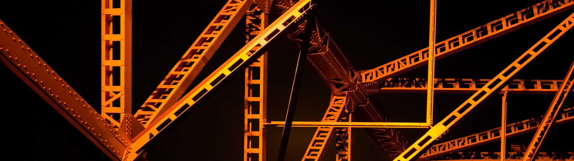 Entramado de vigas metálicas naranjas con celosía sobre fondo negro