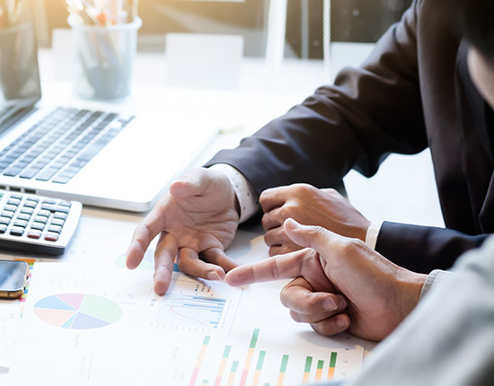 Manos revisando gráficos financieros junto a portátil y calculadora