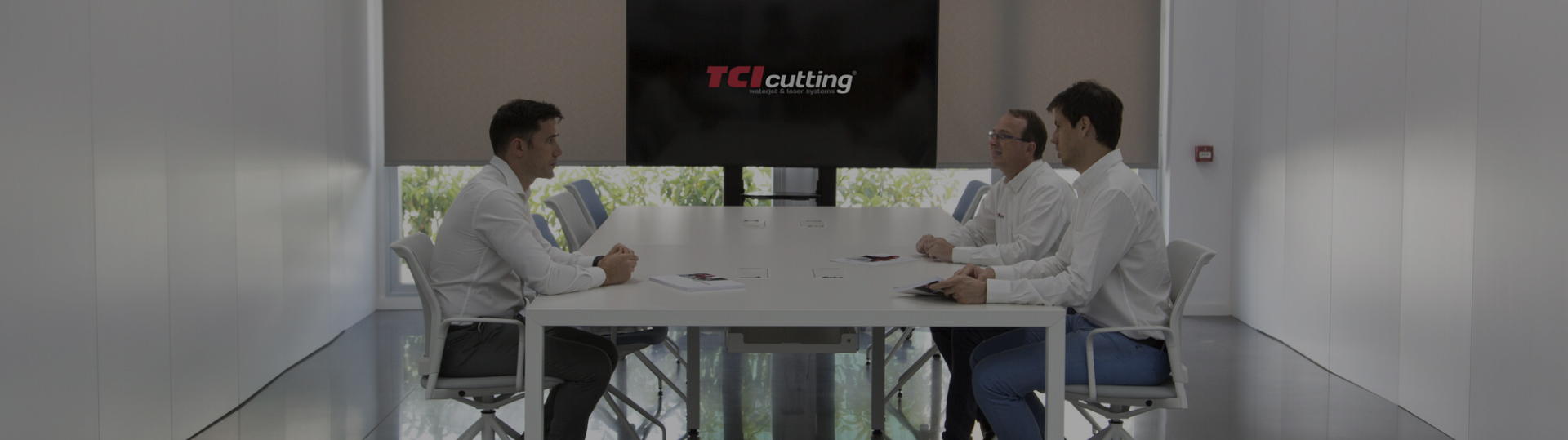 Tres profesionales en reunión técnica frente a pantalla con logo TCI Cutting