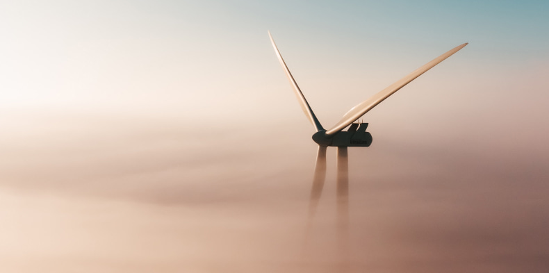 Wind turbine rising above fog at sunrise