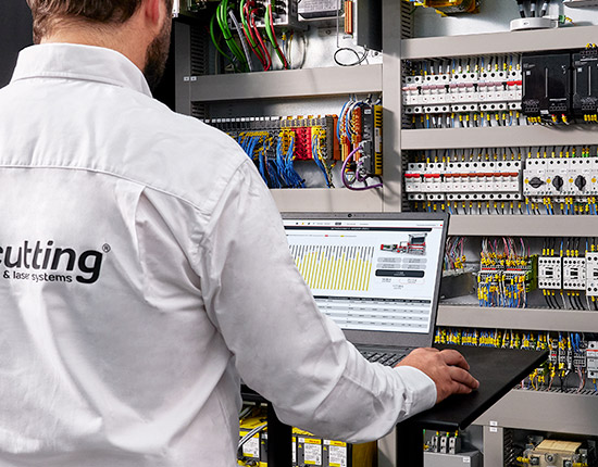 Technician diagnosing machine control cabinet with laptop